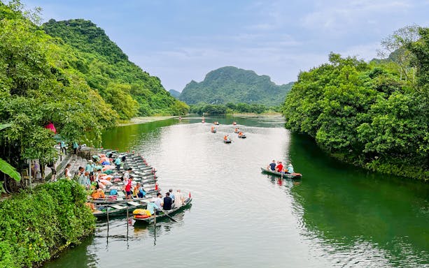 Boat tour on the river at Trang An Landscape Complex, Ninh Binh, Vietnam, surrounded by lush greenery.