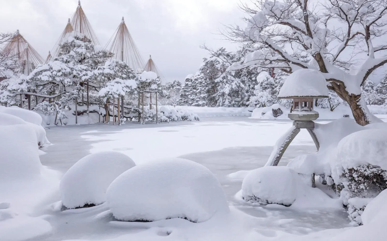 Snow-covered Kenrokuen Garden in Kanazawa during winter, featuring traditional yukitsuri structures.