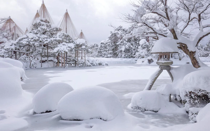 Snow-covered Kenrokuen Garden in Kanazawa during winter, featuring traditional yukitsuri structures.