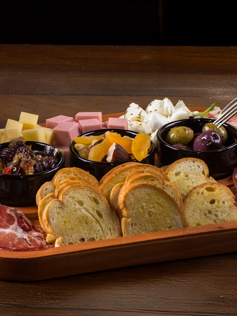 Handmade petiscos platter with cured meats, cheeses, olives, and bread slices.