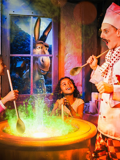Children stirring a cauldron with a chef at Shrek’s Adventure! London, Donkey visible through window.