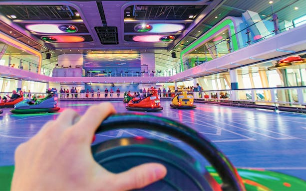 Cruise ship go-kart track with colorful cars and spectators in the background.