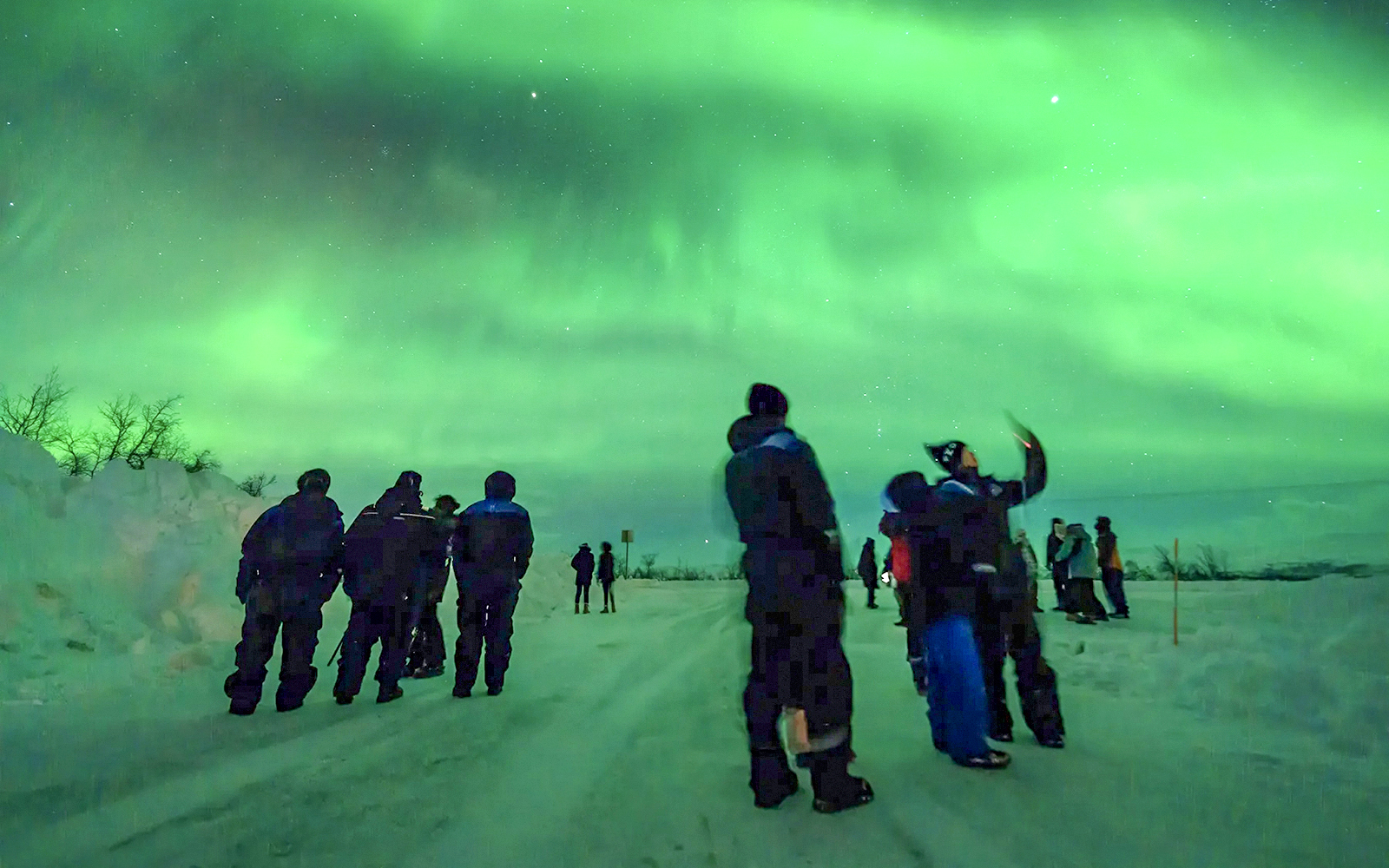 Guests watching Northern Lights during a tour in a snowy landscape.