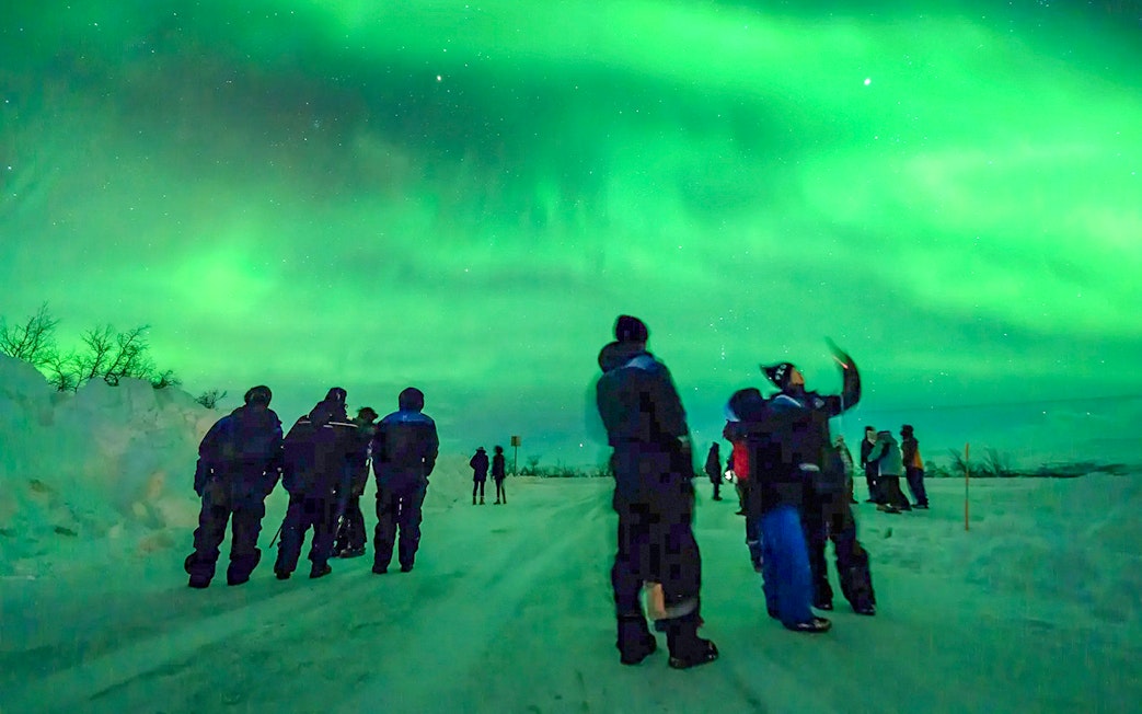 Guests watching Northern Lights during a tour in a snowy landscape.
