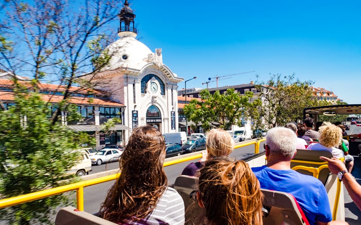Tourists on a hop-on hop-off bus passing Mercado da Ribeira in Lisbon.