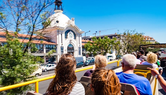 Tourists on a hop-on hop-off bus passing Mercado da Ribeira in Lisbon.