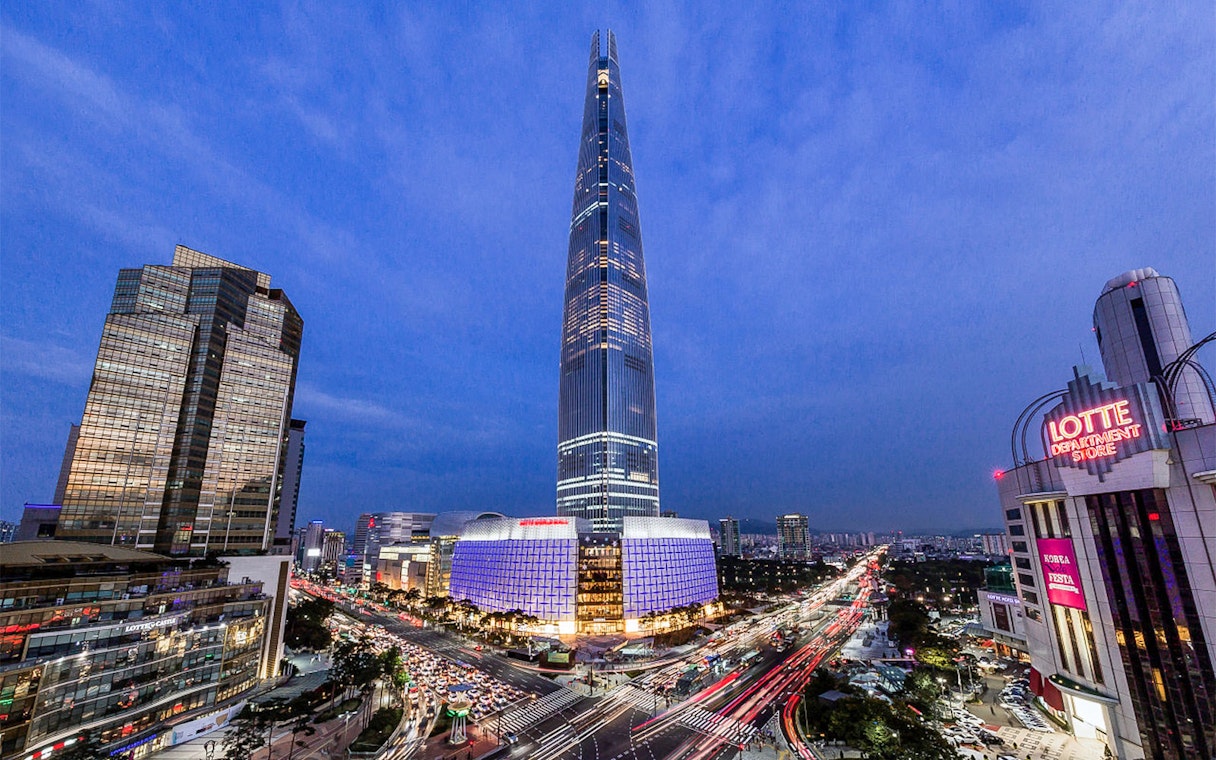 Lotte World Tower illuminated at night in Seoul, with cityscape and traffic below.