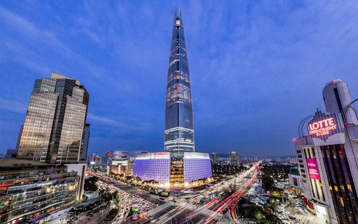 Lotte World Tower illuminated at night in Seoul, with cityscape and traffic below.