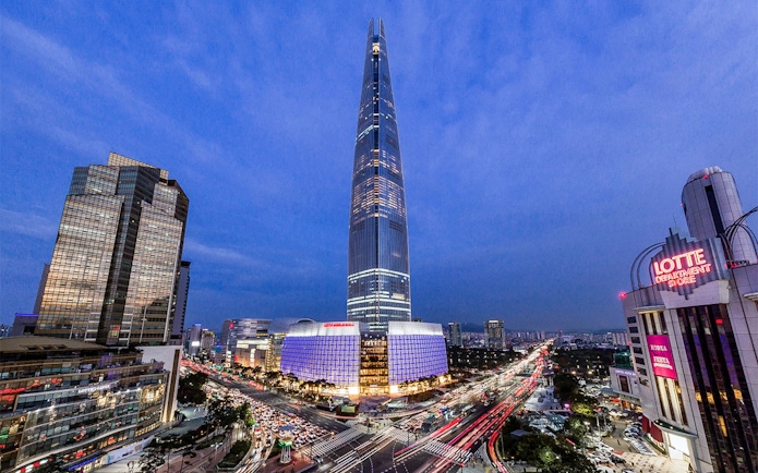 Lotte World Tower illuminated at night in Seoul, with cityscape and traffic below.