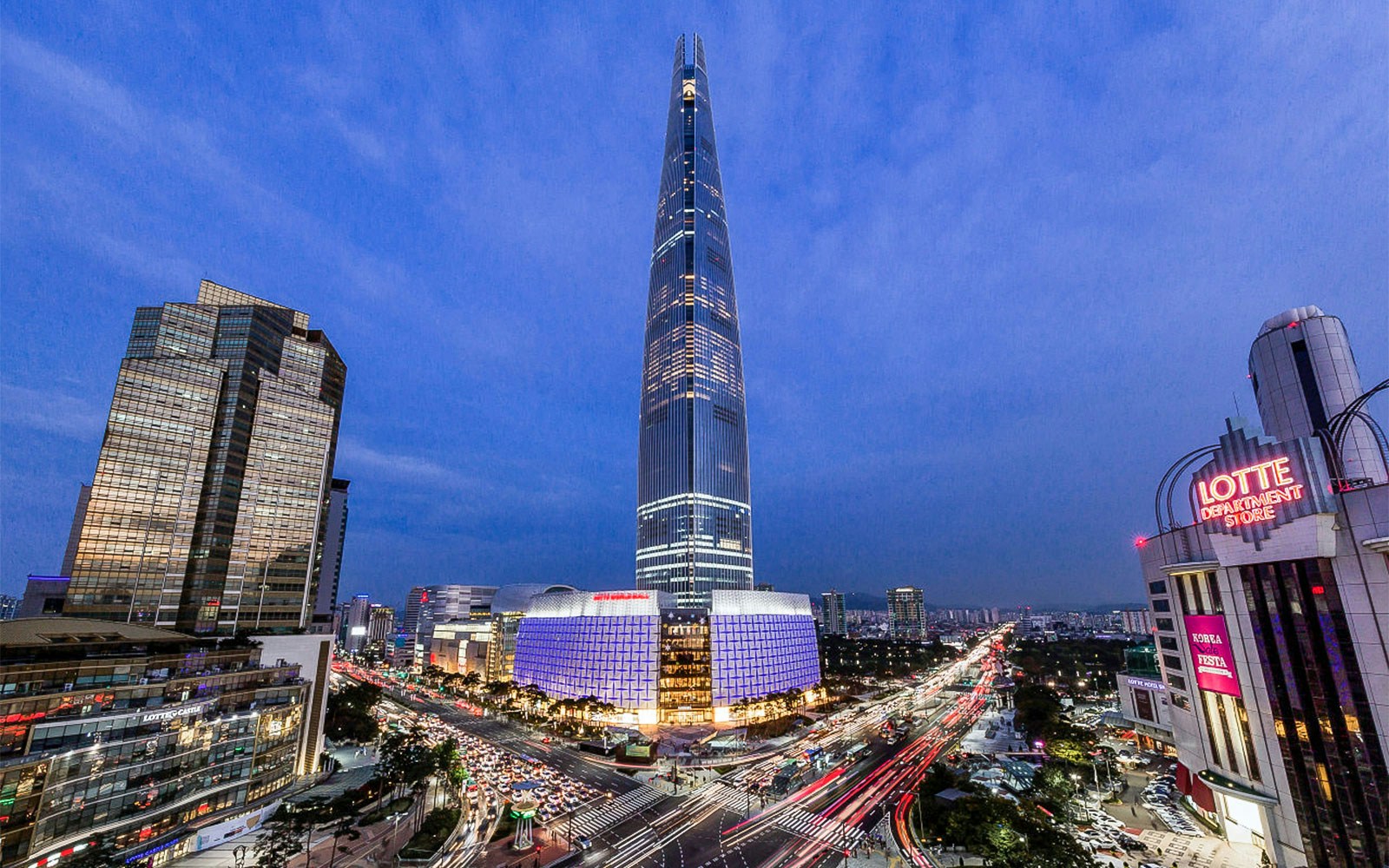 Lotte World Tower illuminated at night in Seoul, with cityscape and traffic below.