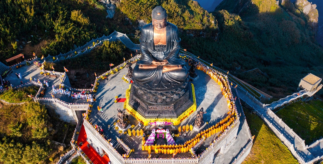 Aerial view of large Buddha statue on Fansipan Mountain, Vietnam, surrounded by visitors.