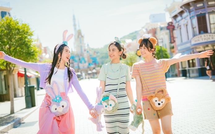 Tourists enjoying a sunny day at Hong Kong Disneyland with plush character bags.
