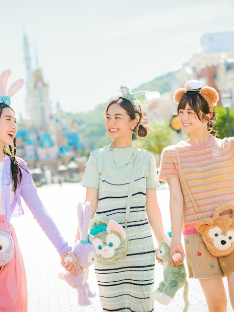 Tourists enjoying a sunny day at Hong Kong Disneyland with plush character bags.