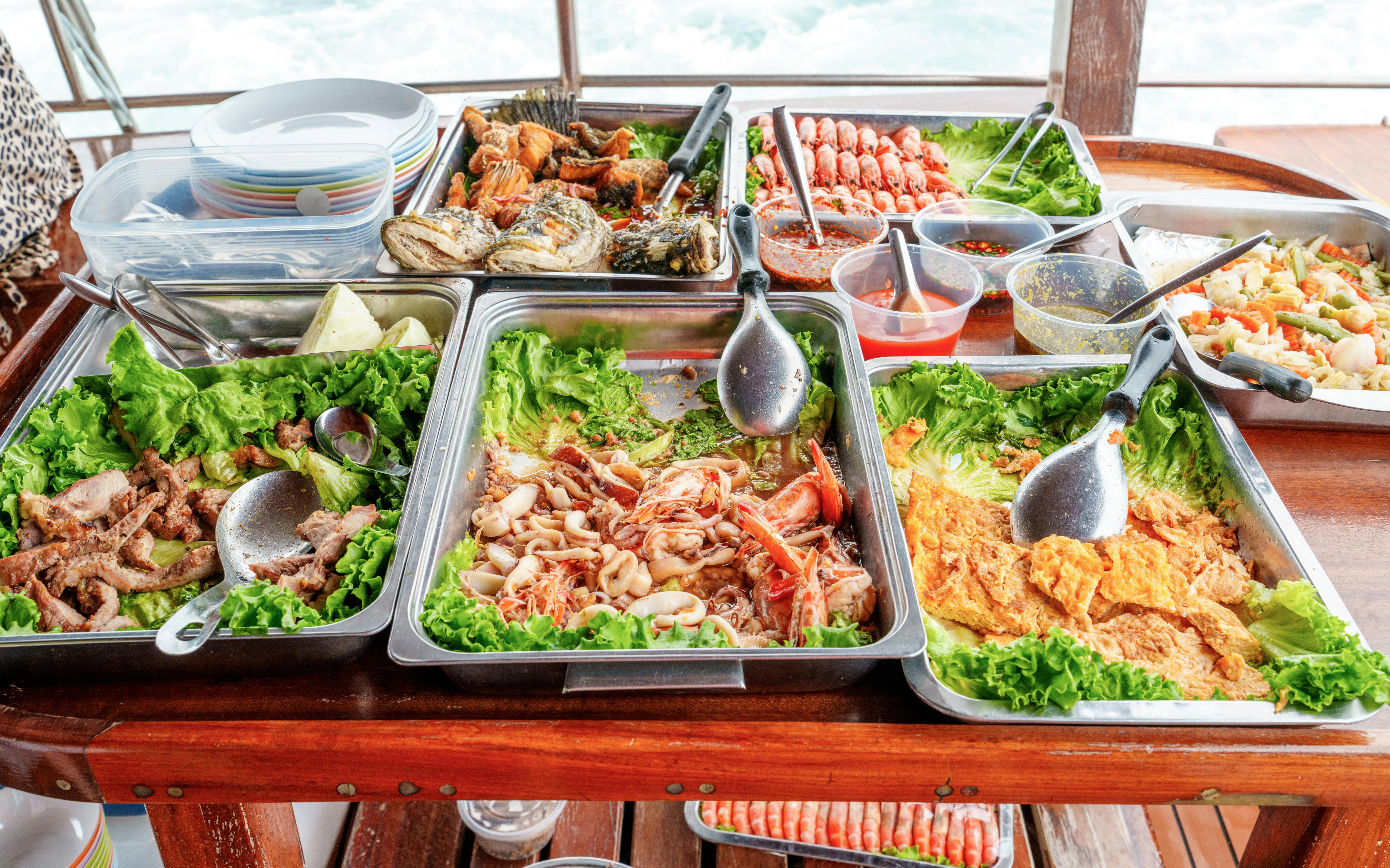Traditional Thai seafood buffet on a boat with fried fish, shrimp, calamari, grilled pork, and vegetables.