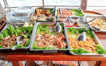 Traditional Thai seafood buffet on a boat with fried fish, shrimp, calamari, grilled pork, and vegetables.