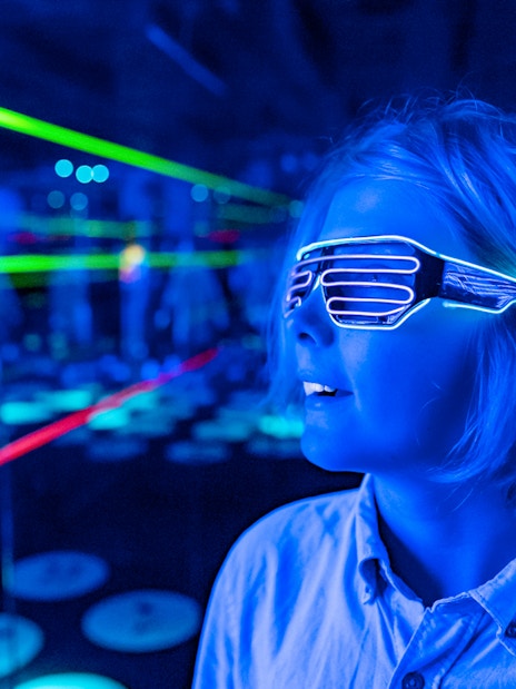 Child wearing LED glasses in a neon-lit room at Infinity Attraction, Gold Coast.
