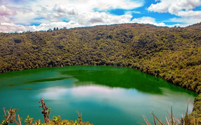 Guatavita Lake surrounded by lush forest under a blue sky in Colombia.