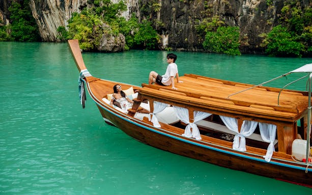 Longtail boat on turquoise water in Krabi with two people relaxing on deck.