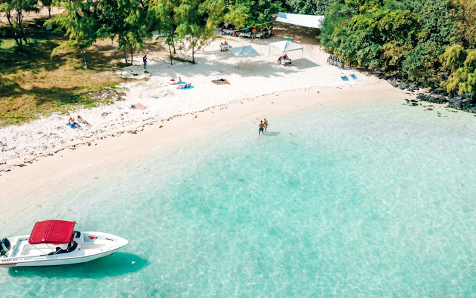 Beachgoers relax on the sandy shore with a boat in the turquoise waters of Côte Est de l'île Maurice.