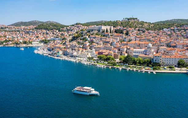 Aerial view of Sibenik Bay, Croatia, with a boat on the water and historic buildings along the coast.