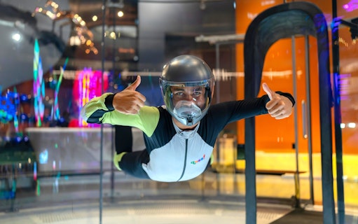 Person experiencing indoor skydiving at iFLY Quest, wearing a flight suit and helmet.