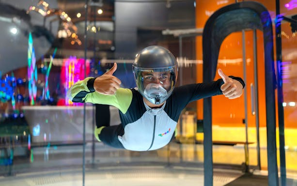 Person experiencing indoor skydiving at iFLY Quest, wearing a flight suit and helmet.