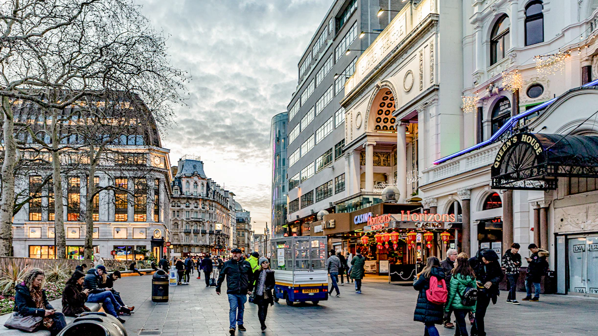 Leicester Square in London with people walking and historic buildings.