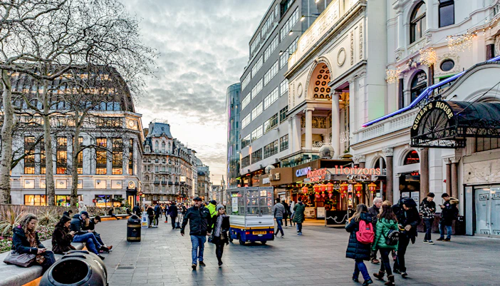 Leicester Square in London with people walking and historic buildings.