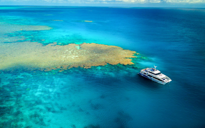 Aerial view of a boat near coral reefs in clear blue waters.