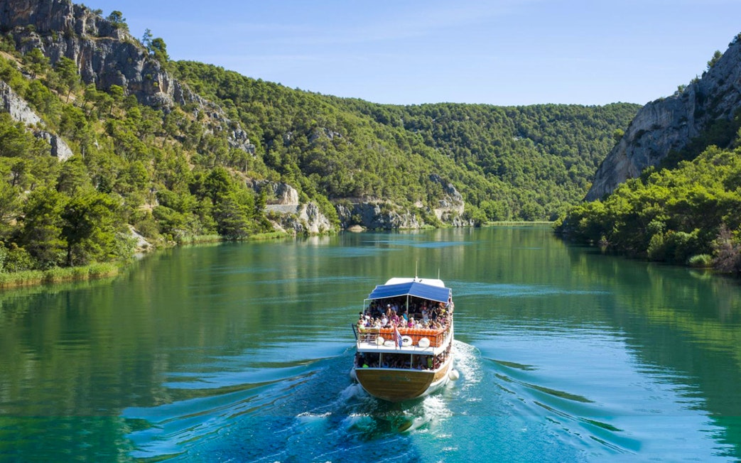 Boat cruising through Krka National Park's lush landscape during guided day trip.