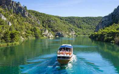 Boat cruising through Krka National Park's lush landscape during guided day trip.