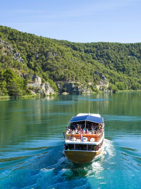 Boat cruising through Krka National Park's lush landscape during guided day trip.