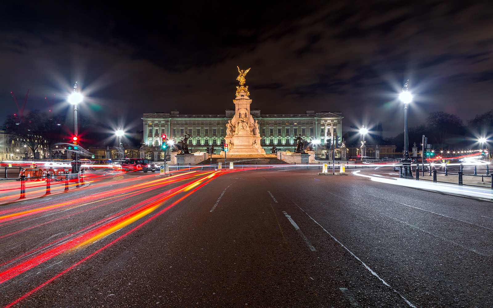 Buckingham Palace illuminated at night with light trails from passing traffic.