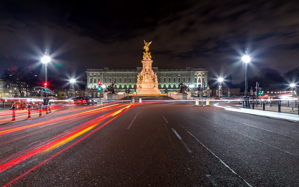 Buckingham Palace illuminated at night with light trails from passing traffic.