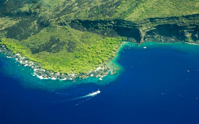 Aerial view of Kealakekua Bay with a boat on the blue water near lush green cliffs.