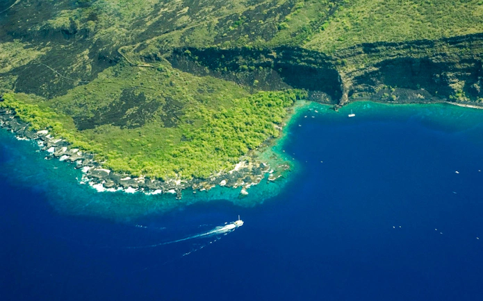 Aerial view of Kealakekua Bay with a boat on the blue water near lush green cliffs.