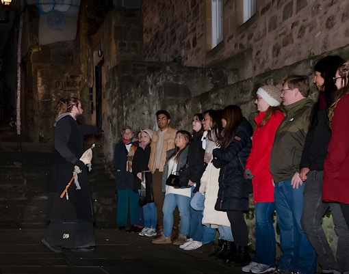 Tour guide leading a group on an Extreme Paranormal Activity Tour in a dimly lit alley.
