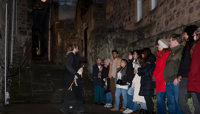 Tour guide leading a group on an Extreme Paranormal Activity Tour in a dimly lit alley.