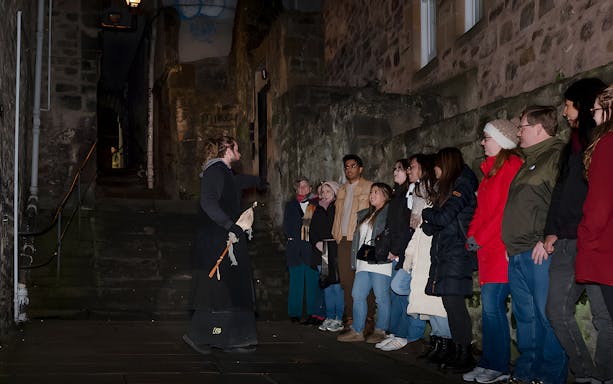 Tour guide leading a group on an Extreme Paranormal Activity Tour in a dimly lit alley.