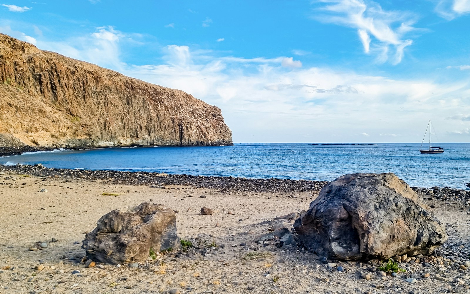 Cliffs and rocky beach at the eastern end of Los Cristianos, Tenerife, with a sailboat in the distance.