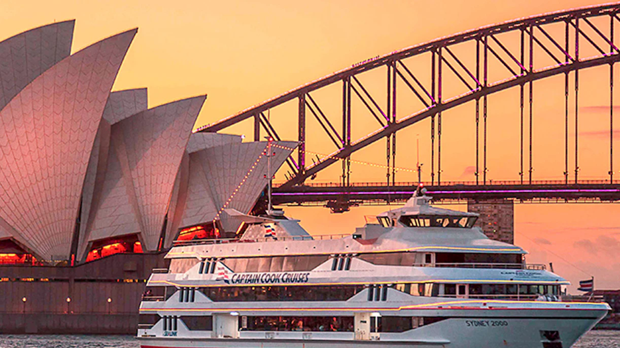 Cruise ship near Sydney Opera House and Harbour Bridge at sunset.