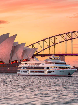 Cruise ship near Sydney Opera House and Harbour Bridge at sunset.