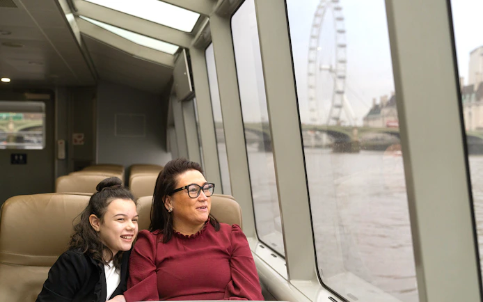 Passengers enjoying Thames River Uber Boat with London Eye view.