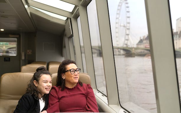 Passengers enjoying Thames River Uber Boat with London Eye view.
