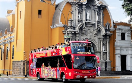 Red double-decker tour bus in front of a historic church in Lima, Peru.
