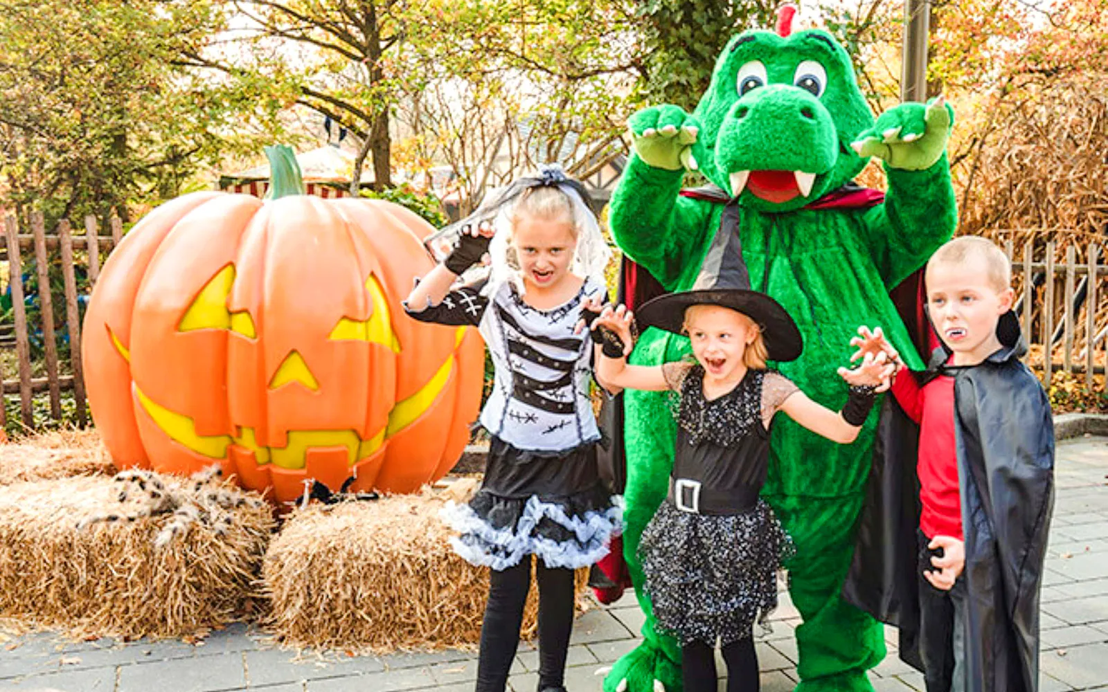 Children in Halloween costumes with a giant pumpkin and mascot at Legoland Billund.
