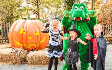 Children in Halloween costumes with a giant pumpkin and mascot at Legoland Billund.