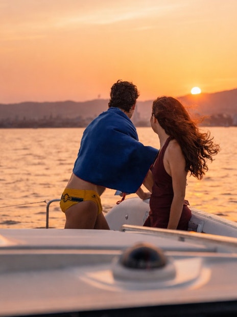 Couple enjoying sunset on a sailing yacht during Barcelona sightseeing cruise.