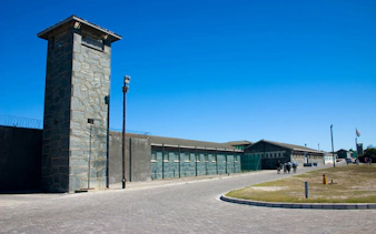 Robben Island Prison entrance with stone watchtower and barbed wire fence.