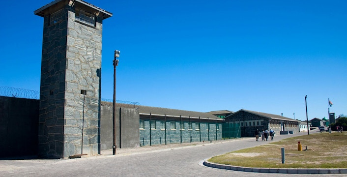 Robben Island Prison entrance with stone watchtower and barbed wire fence.